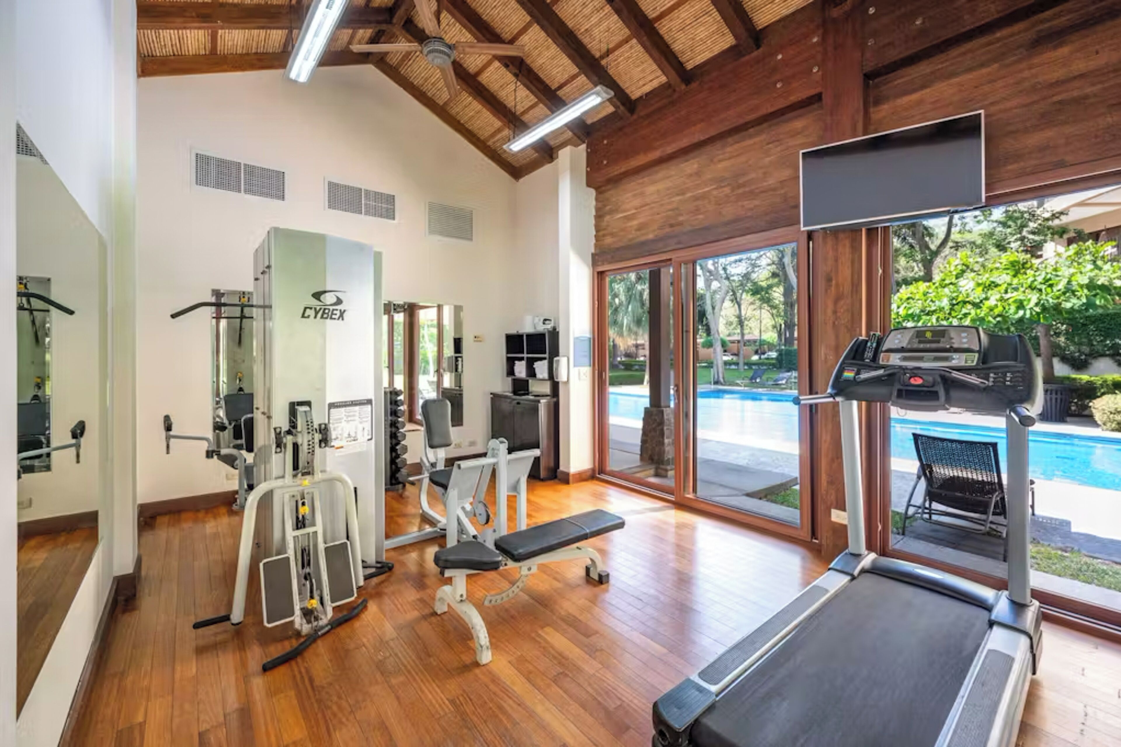 A gym with exercise equipment, a treadmill, and a view of a swimming pool.