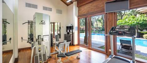 A gym with exercise equipment, a treadmill, and a view of a swimming pool.