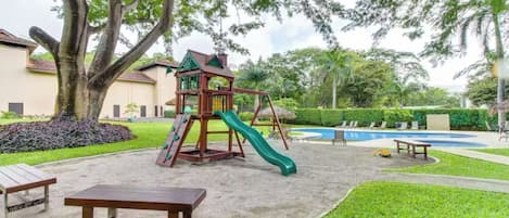 A playground with a slide and climbing structure, a pool, and a picnic table.