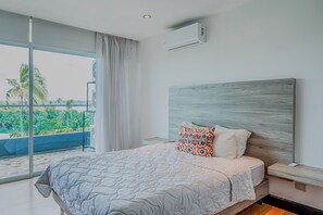 A bedroom with a large bed, a nightstand, a modern air conditioning unit, and a view of palm trees through a sliding glass door. - Ocean-view Stay, El Roble Marina & Pool Access (Puntarenas)