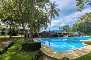 A swimming pool surrounded by lush greenery and a building with a blue roof. - Ocean-view Stay, El Roble Marina & Pool Access (Puntarenas)