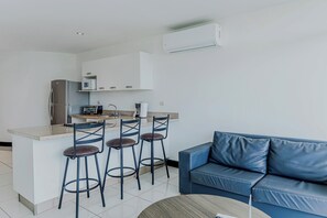 A compact living space with a kitchenette, a blue leather sofa, and a round coffee table. - Ocean-view Stay, El Roble Marina & Pool Access (Puntarenas)