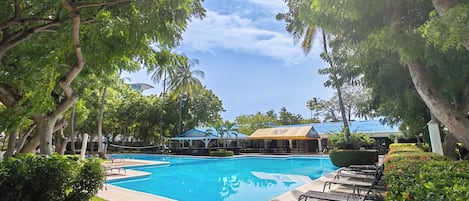 A swimming pool surrounded by trees and a covered area with seating.