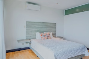 A bedroom with a bed, a nightstand, a wall-mounted air conditioner, and a wooden headboard. - Ocean-view Stay, El Roble Marina & Pool Access (Puntarenas)