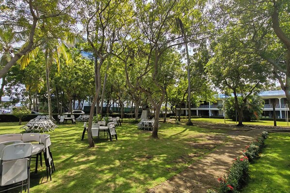 An outdoor seating area with tables and chairs, surrounded by trees and a building in the background. - Ocean-view Stay, El Roble Marina & Pool Access (Puntarenas)