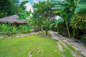 A lush garden with a thatched-roof structure, a variety of tropical plants, and a gravel path. - 4 Mi to Beach! Playa Grande Apartment (Cabo Velas)