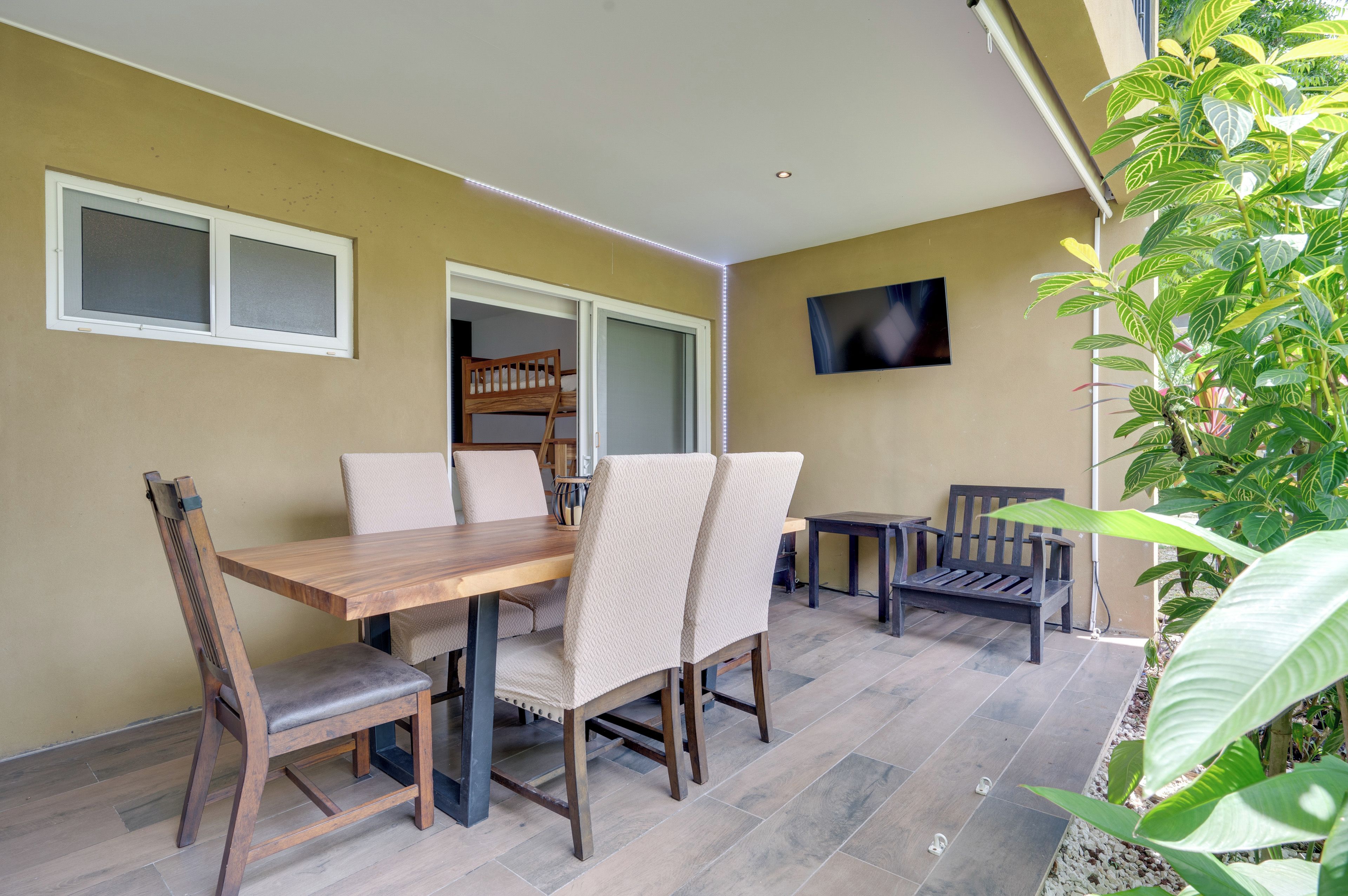 Un coin repas avec une table et des chaises en bois, un téléviseur fixé au mur et une fenêtre donnant sur l’extérieur.
