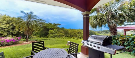 An outdoor patio with a grill, seating, and a view of a lush garden.