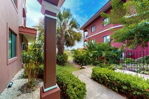 A pathway leading to a building with a red facade, surrounded by lush greenery and a clear sky. - Playa Conchal Resort Condo w/ Ocean View (Cabo Velas)