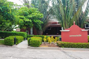 Un edificio rojo con un letrero que dice 'Arrecachillo', rodeado de exuberante follaje y palmeras.