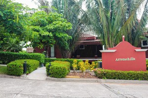 A red building with a sign reading 'Arrecachillo' surrounded by lush greenery and palm trees.