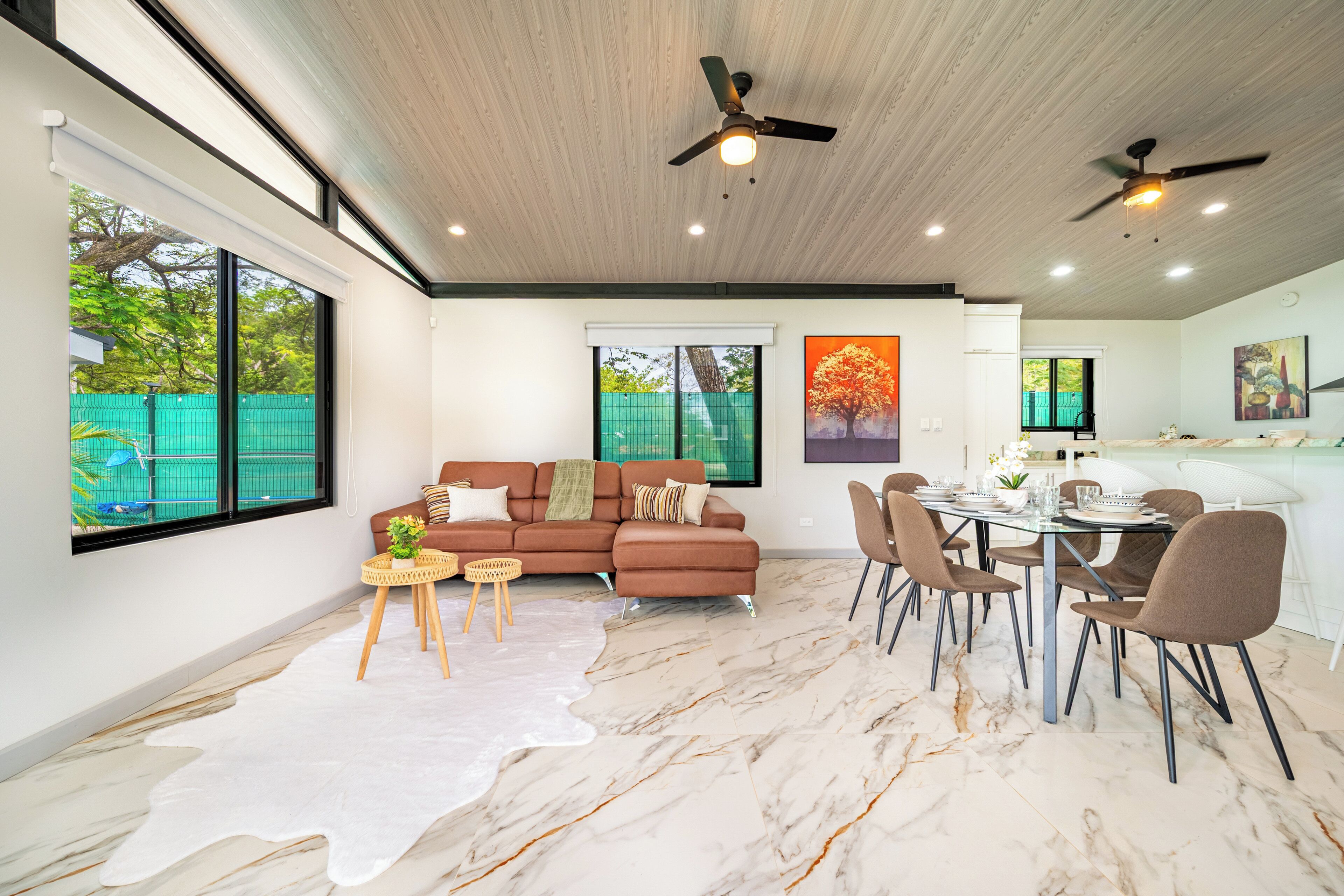 A modern living room with a sofa, dining table, chairs, and a ceiling fan.