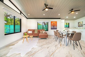 A modern living room with a sofa, dining table, chairs, and a ceiling fan.