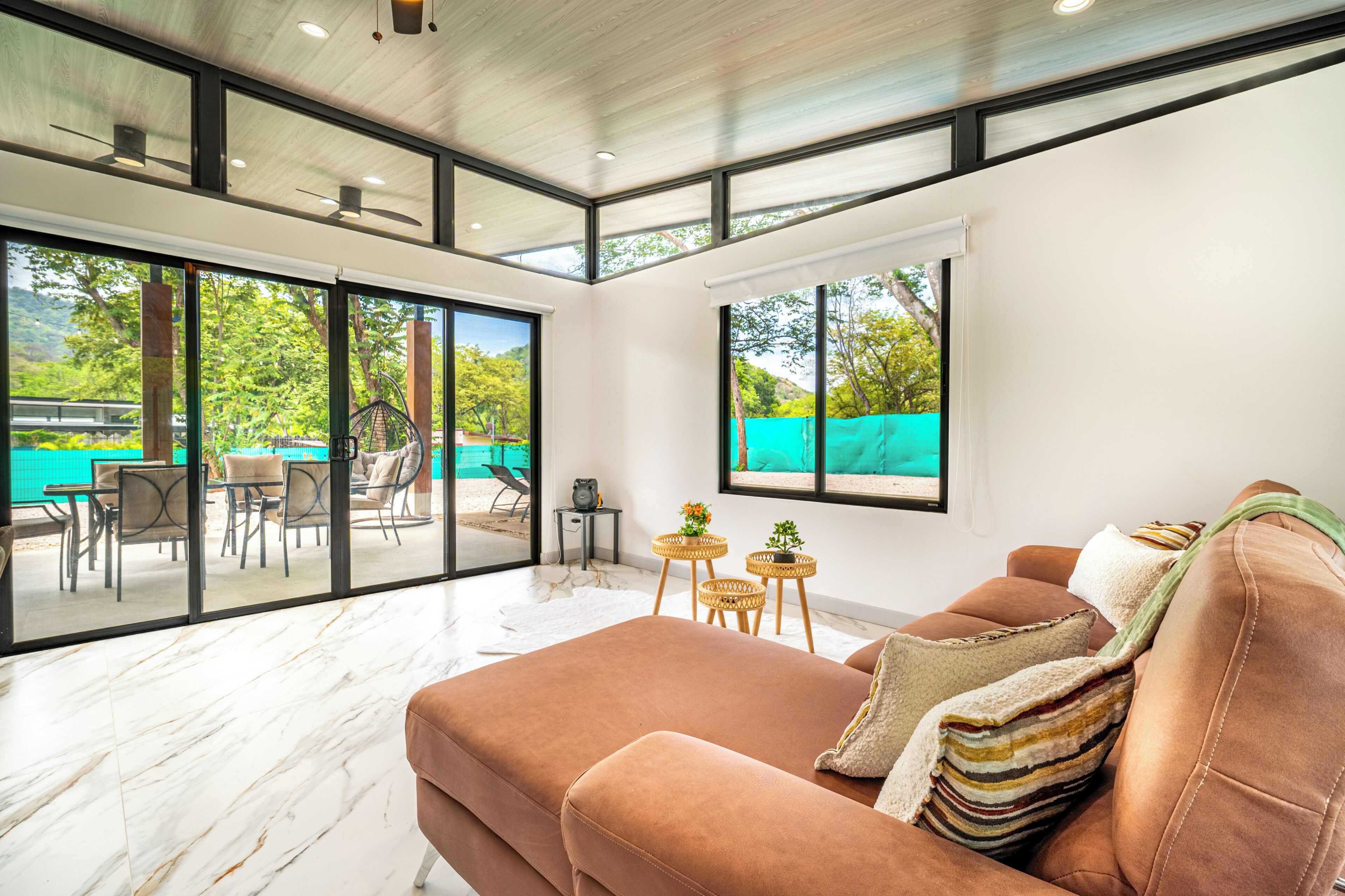 Un salon moderne avec un grand canapé, un téléviseur et une vue sur un espace extérieur comprenant une piscine et des fauteuils.