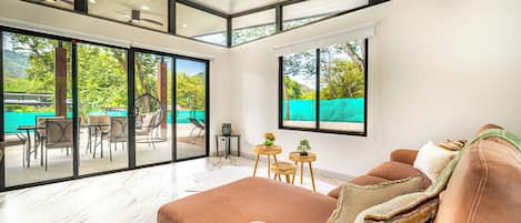 Un salon moderne avec un grand canapé, un téléviseur et une vue sur un espace extérieur comprenant une piscine et des fauteuils.