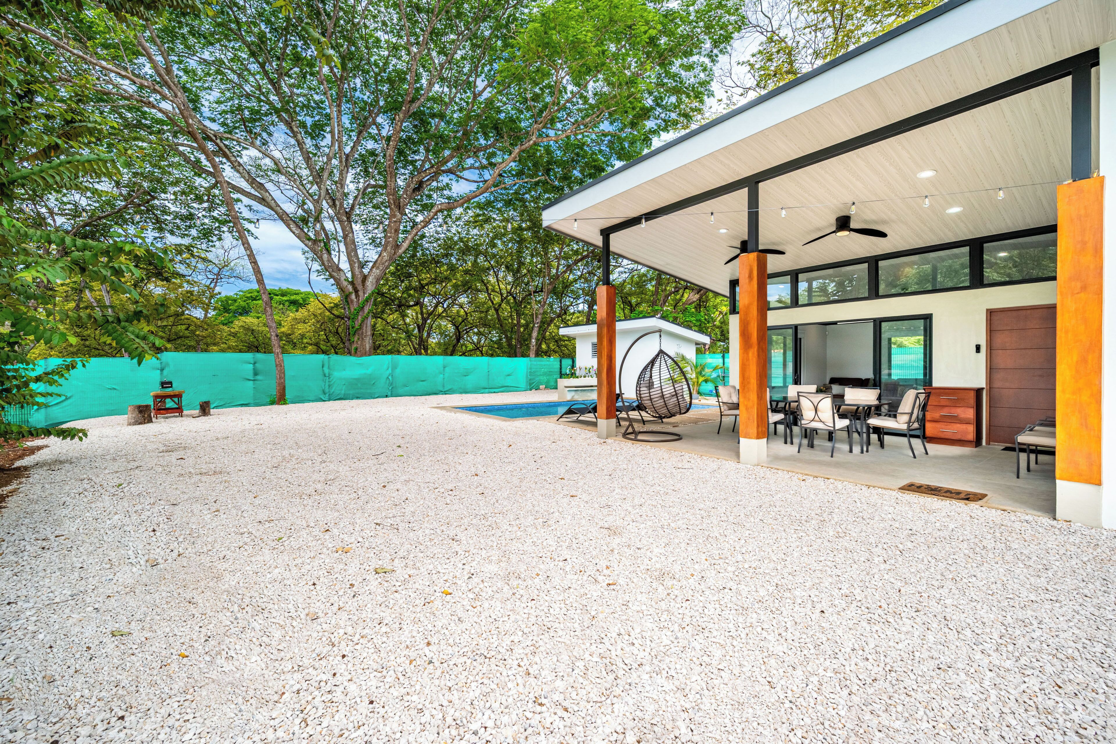 A modern outdoor patio with a pool, seating area, and a covered section with tables and chairs.