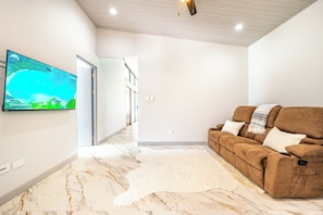 Una sala de estar moderna con un televisor de pantalla plana montado en la pared, un sofá de cuero marrón con cojines, una alfombra esponjosa blanca y un piso de mármol.