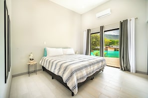 A bedroom with a bed, a nightstand, a potted plant, and a view of a green landscape through the window.