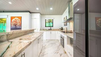 A modern kitchen with white cabinets, marble countertops, and a central island.