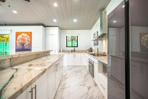 Una cocina moderna con armarios blancos, encimeras de mármol y una isla central.
