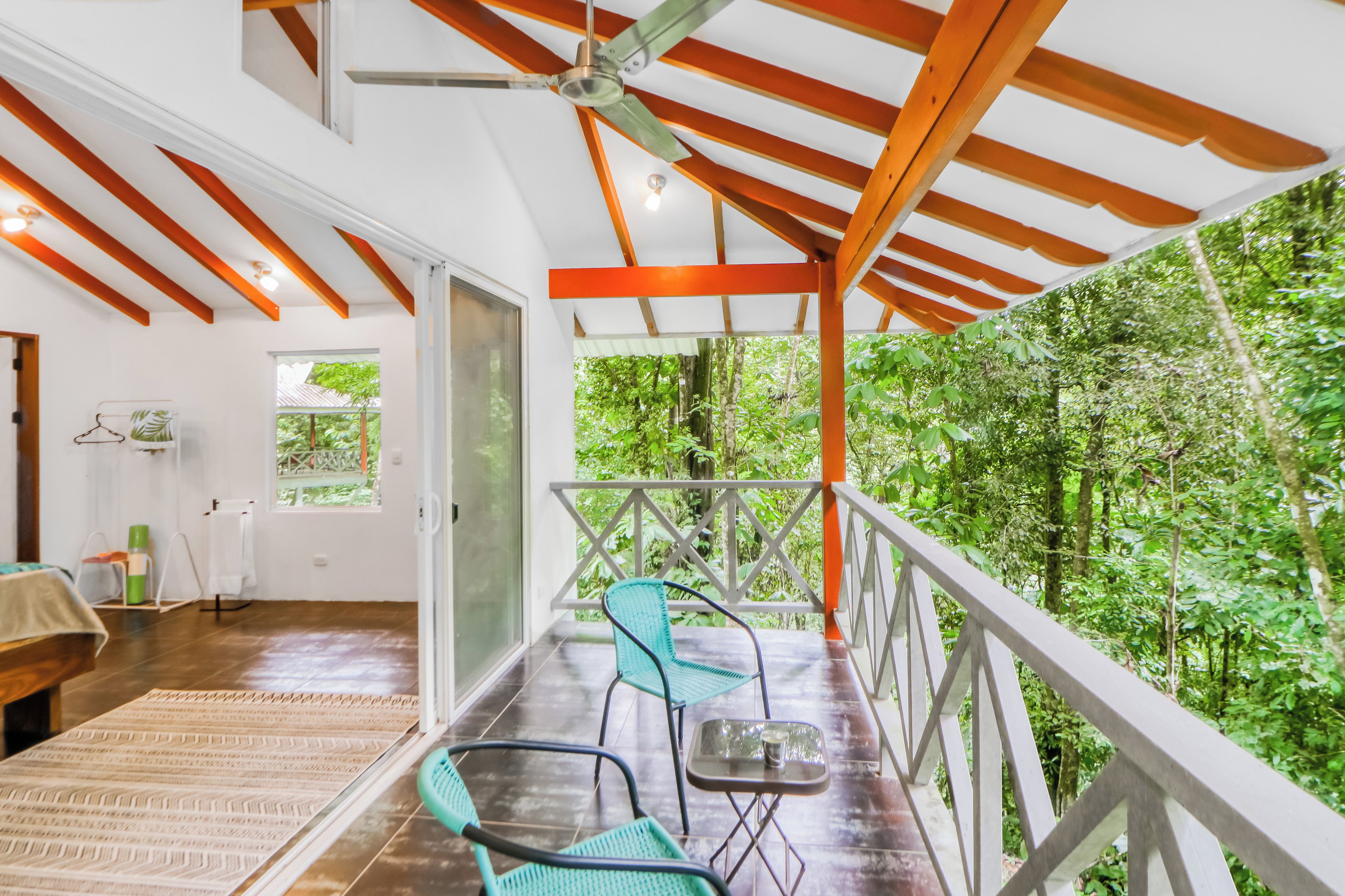 A room with a wooden ceiling, a balcony with a railing, and a view of a forest.