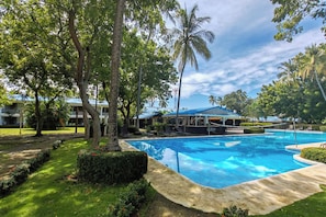 A swimming pool surrounded by lush greenery and palm trees, with a building in the background. - Puerto Azul Marina, Pool & On-site Dining (Puntarenas)