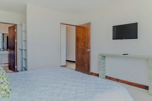 A bedroom with a bed, a TV mounted on the wall, a wooden wardrobe, and a small desk with a mirror. - Puerto Azul Marina, Pool & On-site Dining (Puntarenas)