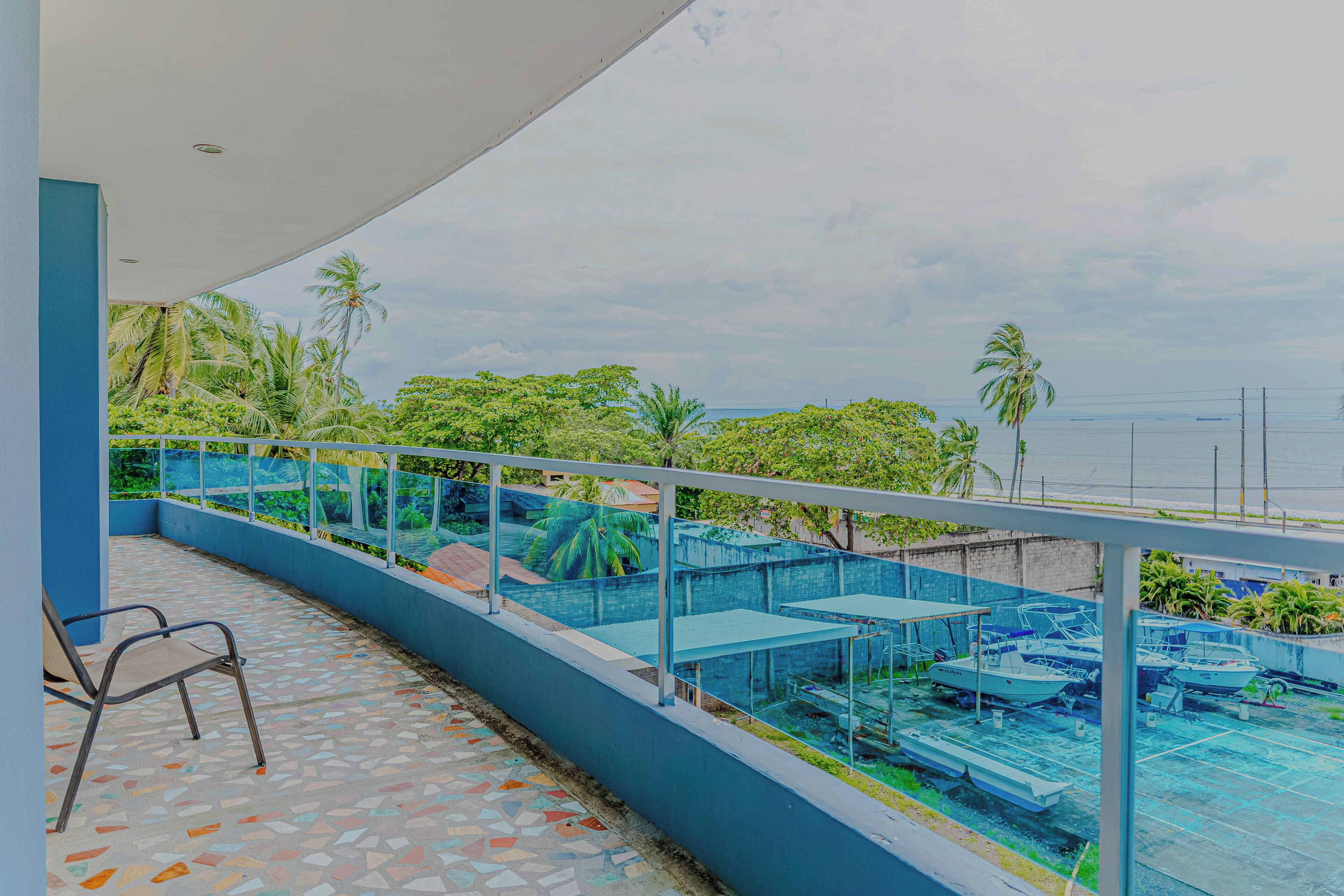 A balcony with a tiled floor, metal chairs, and a view of boats and greenery.
