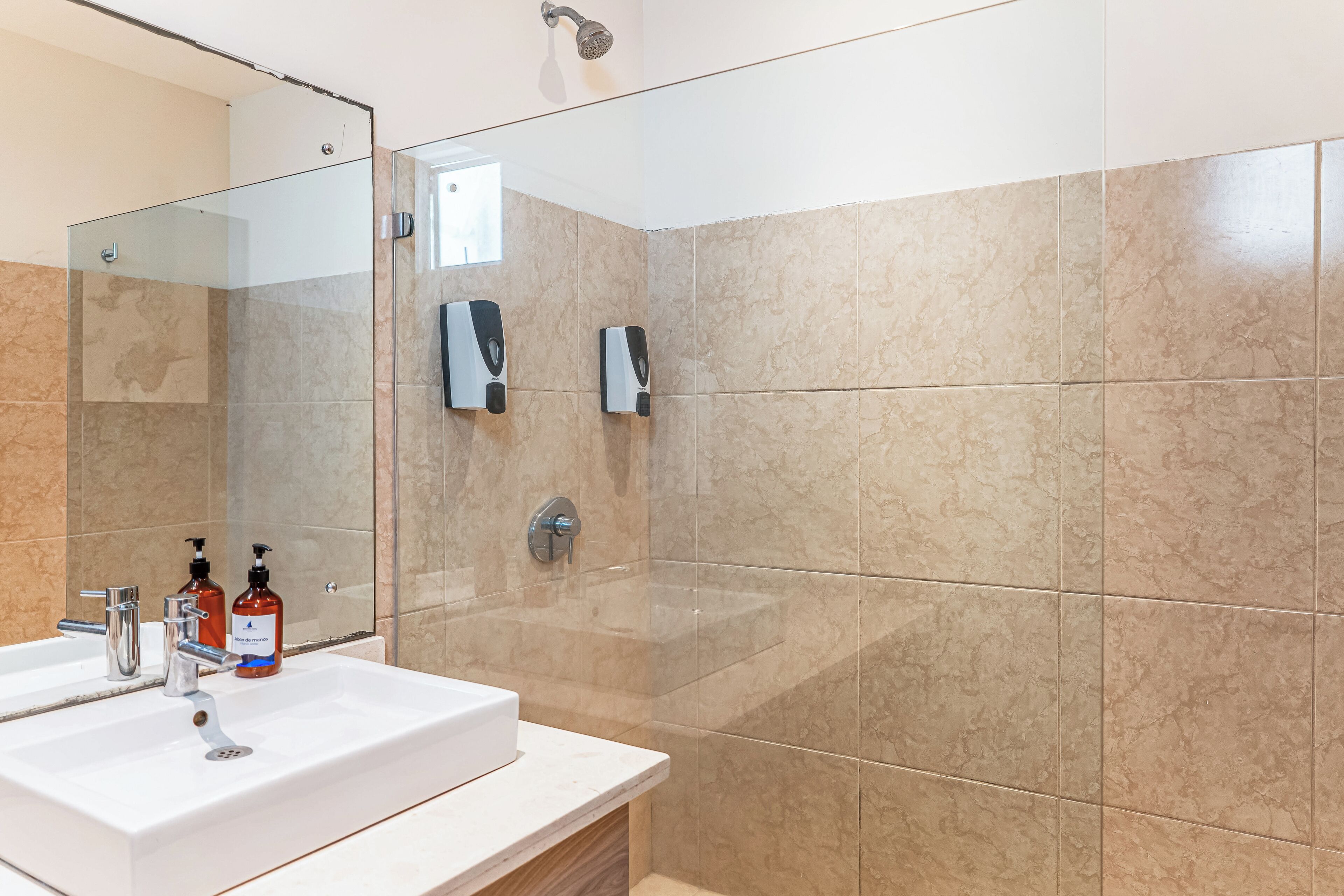 A modern bathroom with a glass shower enclosure, a white sink, and two hand soap dispensers.