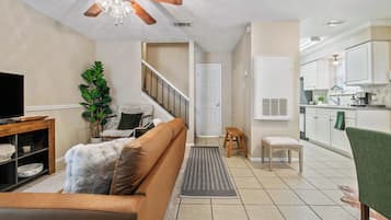 A living room with a sofa, a television, a ceiling fan, a staircase, and a kitchen area with cabinets and a sink.