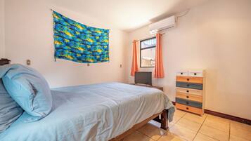 A bedroom with a bed, a wall-mounted TV, a dresser, and a window with curtains.