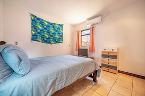 A bedroom with a bed, a wall-mounted TV, a dresser, and a window with curtains.