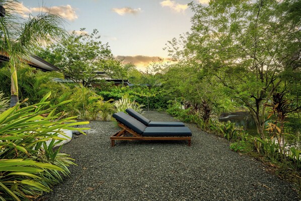 A secluded outdoor seating area with a lounge chair and a small table, surrounded by lush greenery and a pebble path. - Tamarindo Home w/ Pool, 2 Mi to Beach! (Tamarindo)
