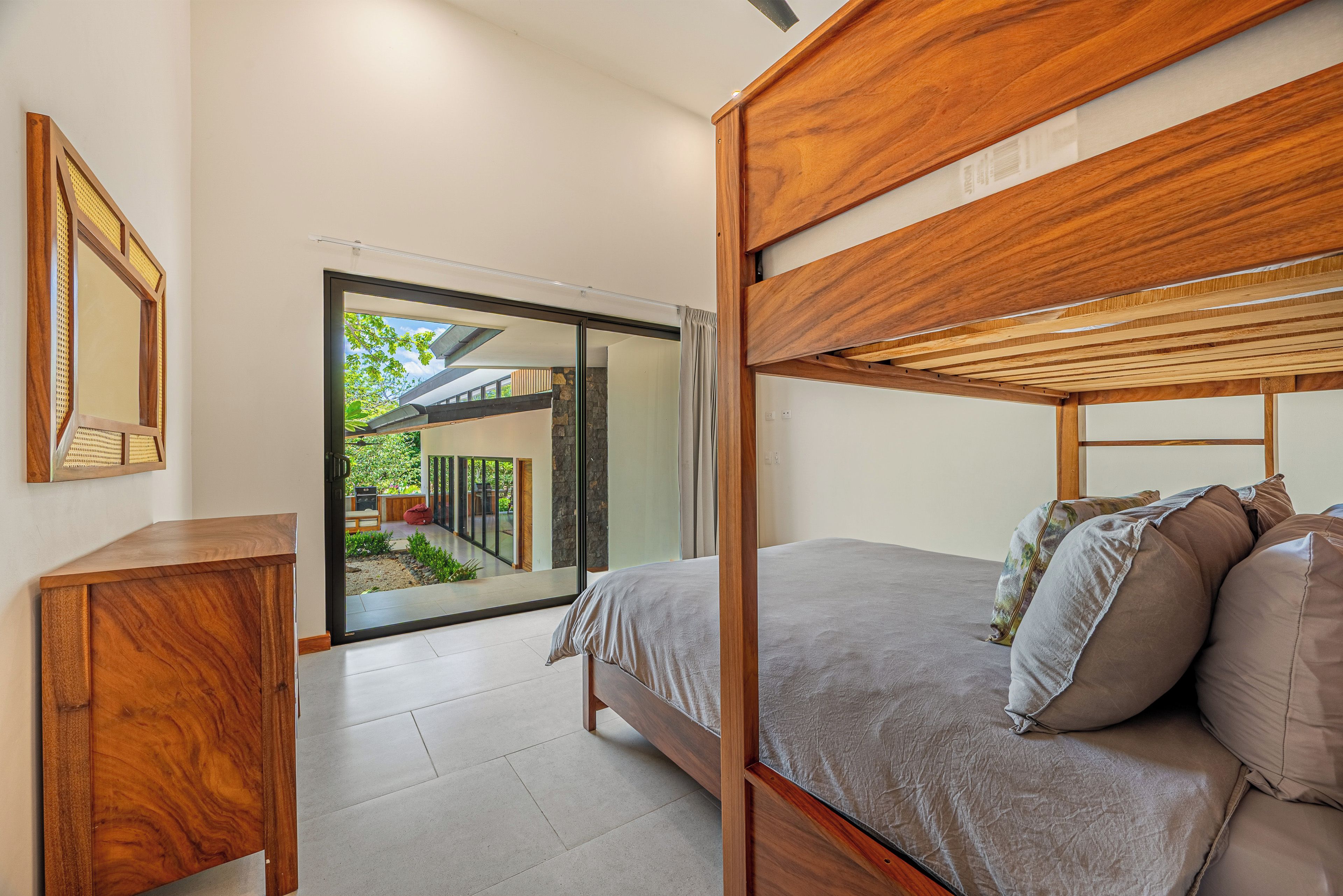 A modern bedroom with a wooden bunk bed, a bedside table, and a large window offering a view of the outdoors.