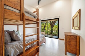 A bunk bed with a wooden frame, a bedside table, and a view of greenery through a glass door. - Tamarindo Home w/ Pool, 2 Mi to Beach! (Tamarindo)