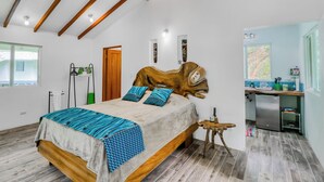 Ein Schlafzimmer mit geneigter Decke, einem Bett mit blau gemusterten Textilien, einem Holz-Kopfteil und einem kleinen Holzschemel.