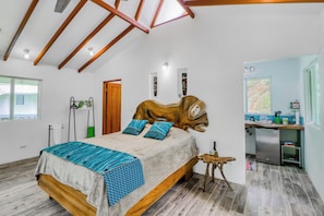 A bedroom with a sloped ceiling, a bed with blue patterned bedding, a wooden headboard, and a small wooden stool. - Off-grid Ojochal Studio w/ Pool & Trail Access! (Ciudad Cortés)
