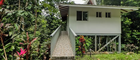 A two-story building with a staircase leading to a balcony, surrounded by lush greenery.