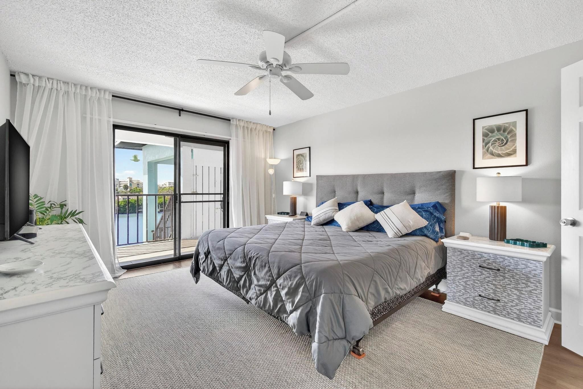 A modern bedroom with a large bed, a ceiling fan, and a view of the outdoors.