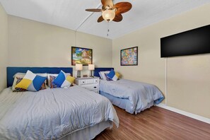 Une chambre avec deux lits, un ventilateur de plafond, des tables de chevet, des lampes et deux tableaux encadrés au mur.