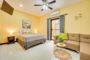A hotel room with a bed, a sofa, a small table with a plant, a ceiling fan, and an air conditioning unit. - Family Retreat w/ Pool Access: Walk to Beach! (Sardinal)