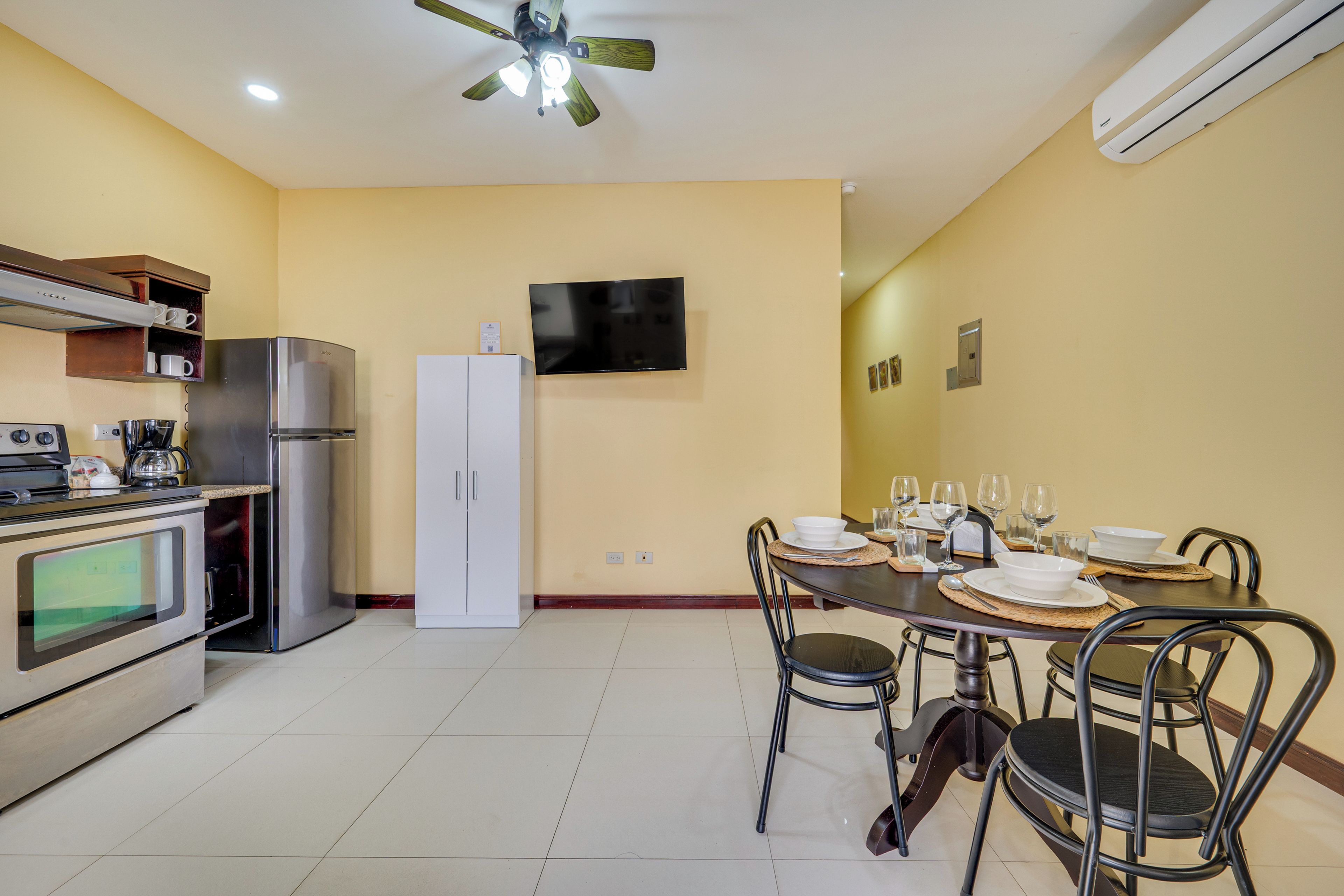 Une cuisine compacte dotée d’appareils électroménagers modernes, un coin repas avec une table pour quatre personnes et un téléviseur à écran plat fixé au mur.
