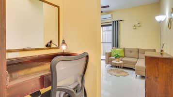 Una habitación con escritorio de madera, una silla, un sofá y una mesita con una planta.