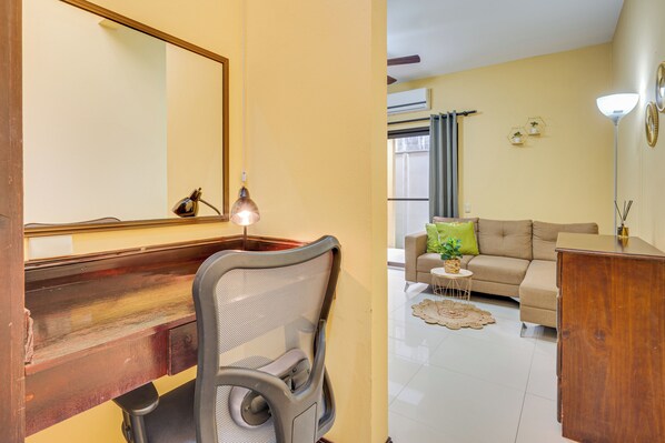 A room with a wooden desk, a chair, a sofa, and a small table with a plant.