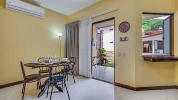 Un coin repas avec une table dressée pour quatre personnes, des chaises, une horloge et une vue sur l’extérieur, visible à travers une porte ouverte.