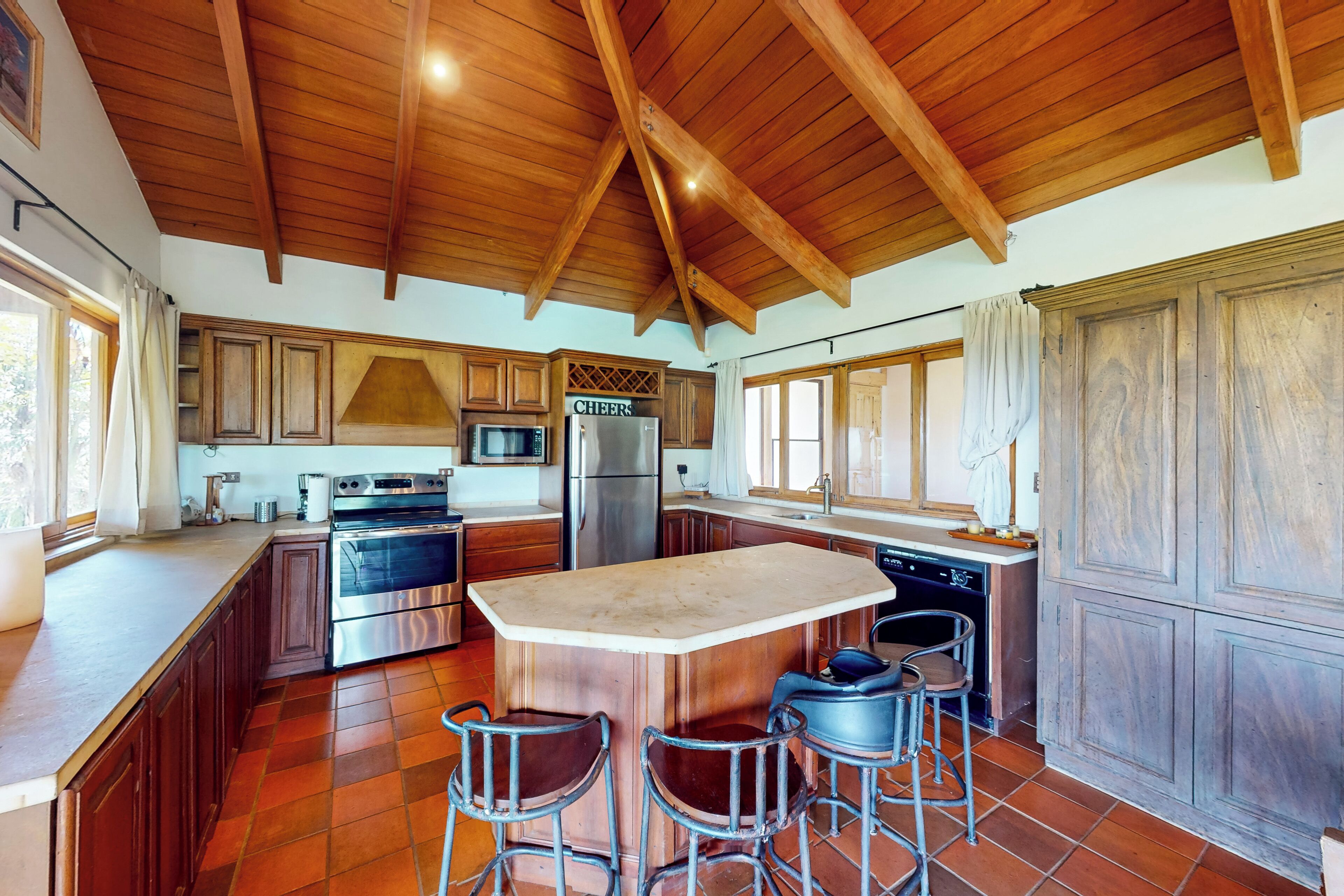 A spacious kitchen with wooden beams, a large island, bar stools, and modern appliances.