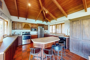 A spacious kitchen with wooden beams, a large island, bar stools, and modern appliances.