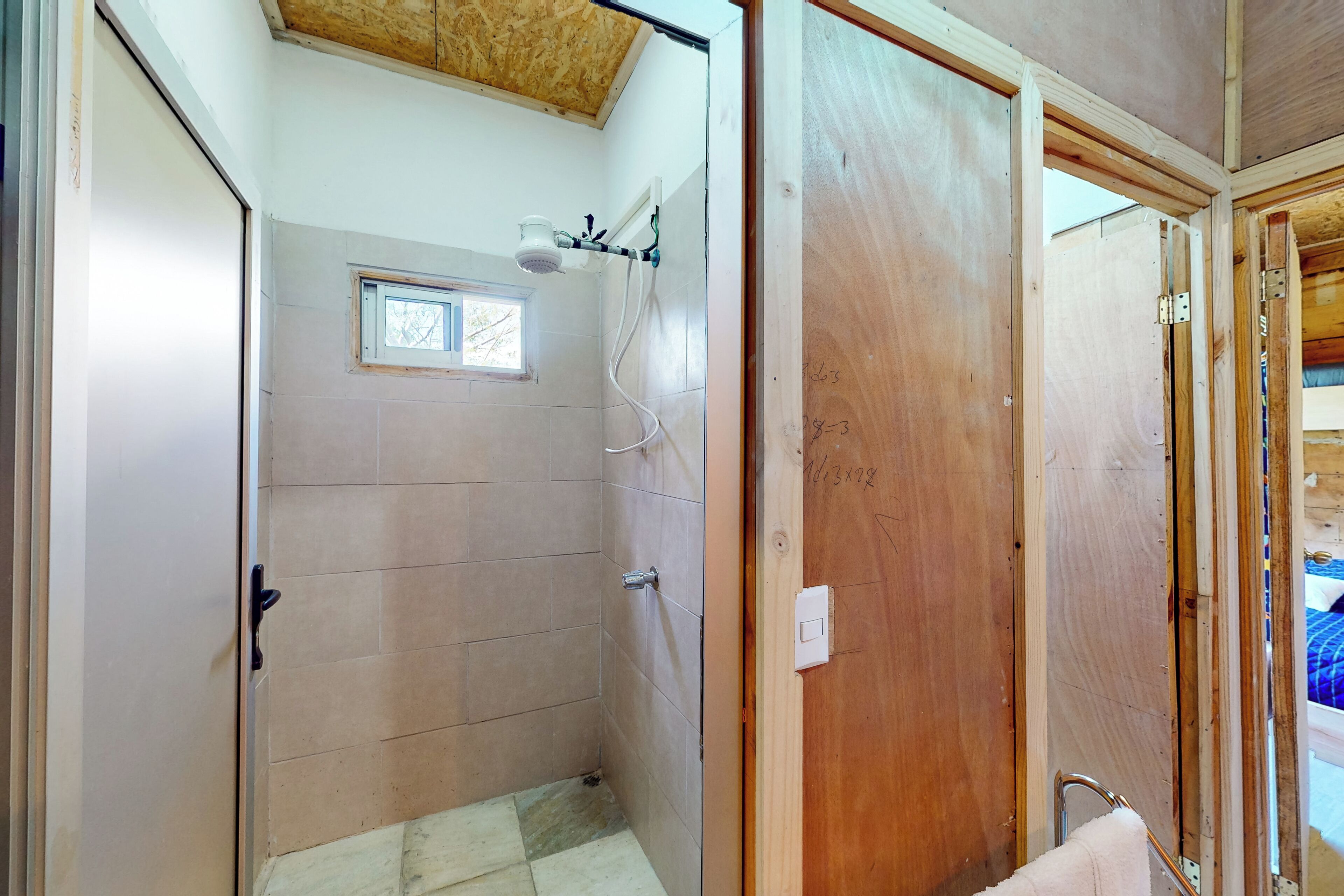 A bathroom with a shower, a window, and a wooden door.