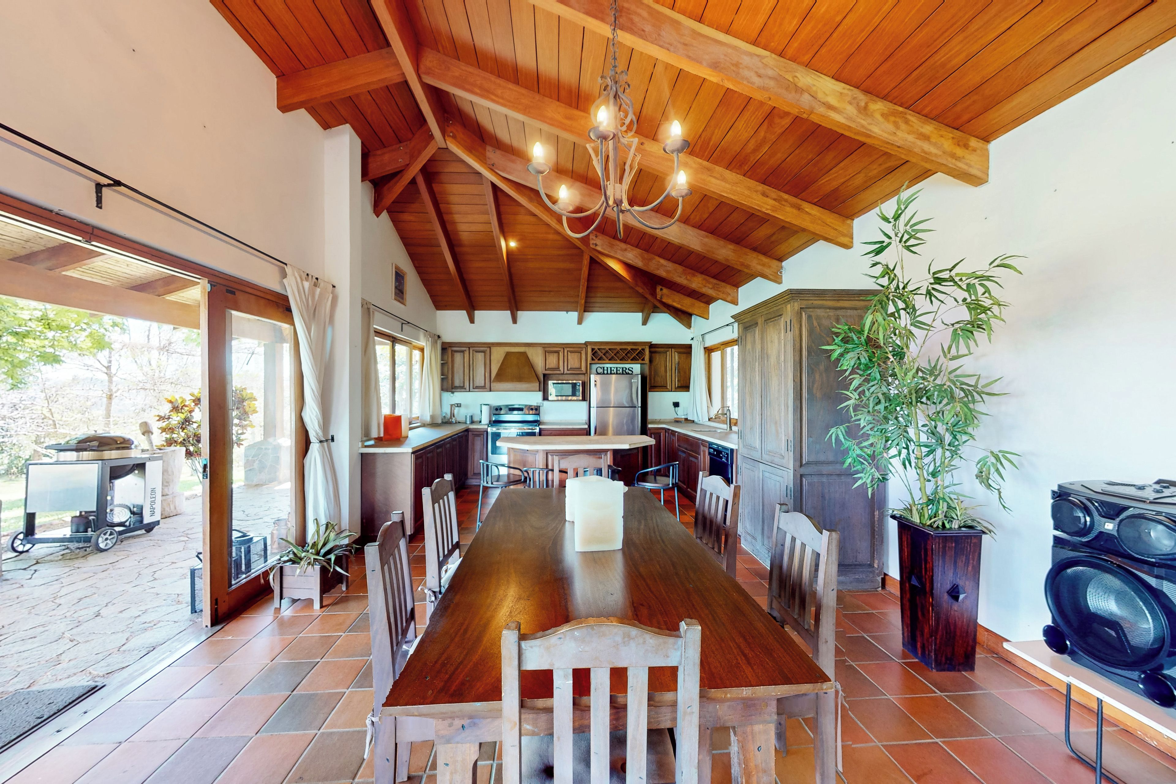 A spacious kitchen with wooden beams, a dining table with chairs, and a large potted plant.