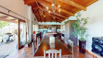 A spacious kitchen with wooden beams, a dining table with chairs, and a large potted plant.